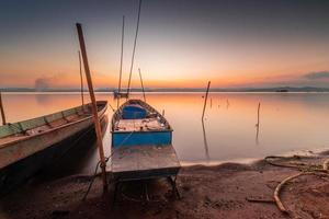 dos pequeño barcos amarrado en el apuntalar de el lago. a puesta de sol hermosa ligero foto