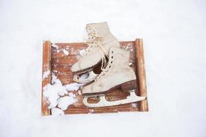 Old vintage skates on the snow.A pair of white skates on a wooden snow-covered board. photo