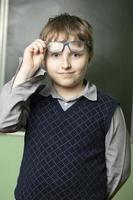 Portrait of a funny schoolboy in glasses at the blackboard. Ten year old student in class. photo