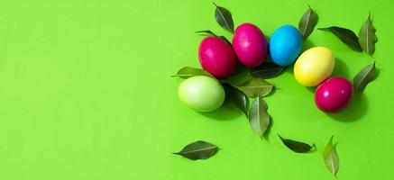 Eggs painted in different colors and a scattering of green leaves on a green background. Copy space for text. Postcard. photo