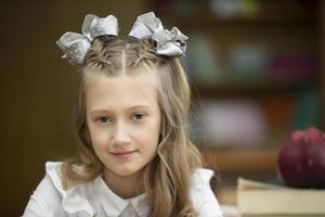 hermosa Chica de escuela con arcos a su escritorio. niña en el salón de clases con libros y un manzana. secundario escuela. espalda a escuela. foto