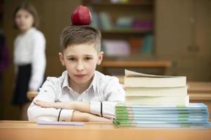 Funny schoolboy at the desk. The boy in the class is playing around, put an apple on his head. Secondary school. Teaching extraordinary children. photo