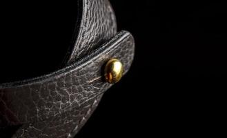 Part of a leather product or belt with a metal rivet on a black background. photo