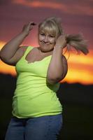 A plump middle-aged woman poses in jeans and a bright t-shirt against the background of the evening sky, overweight xxl. A full girl enjoys life. photo