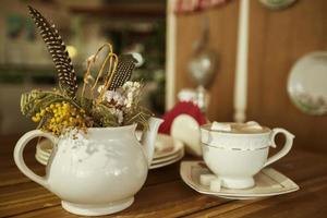 On a table in a cafe there is a vase with flowers and exotic feathers and a cup of coffee. photo