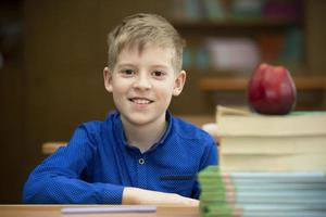 Schoolboy at the desk. Boy in the classroom with books and an apple. Secondary school. Back to school. photo