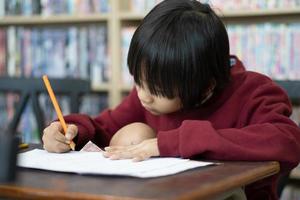 Asian boy writing in notebook, doing homework in a classroom at school. Education concept. photo