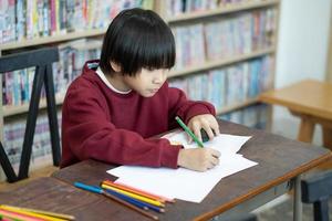 Asian boy writing in notebook, doing homework in a classroom at school. Education concept. photo