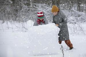 Two boys are playing in the snow. Children sculpt from snow. Play on a winter day in nature. photo