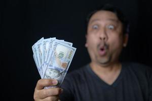 Asian handsome man holding bunch of dollars banknotes on black background photo