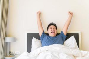 Portrait of asian obese boy awaking, wake up on the bed. photo