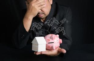 paper house and piggy bank on hand on black background, Businessman stressed photo