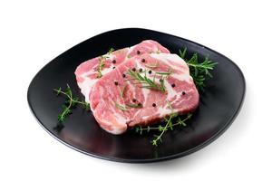 Pieces of pork meat with rosemary and thyme leaves on black dish on white background, photo