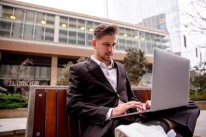 A young guy in a suit works on a computer in the park, looks into a computer photo