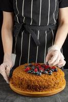 A female chef decorates a homemade carrot cake with fresh berries on a dark background photo