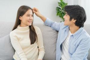 Happy, smile asian young couple love spending free time together, bonding to each other and smiling romantic sitting on couch in living room at home. Weekend leisure activity of family lifestyle.