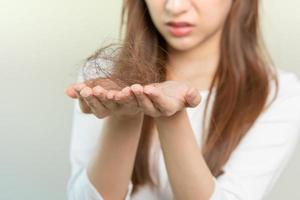 grave, preocupado asiático joven mujer, niña participación cepillar, espectáculo su peine, cepillo para el pelo con largo pérdida pelo problema después cepillado, pelo otoño fuera en su mano en vivo habitación. salud cuidado, belleza tratamiento. foto