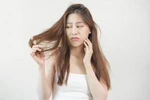 Damaged Hair, frustrated asian young woman, girl hand in holding splitting ends, messy unbrushed dry hair with face shock, long disheveled hair, health care of beauty. Portrait isolated on background. photo