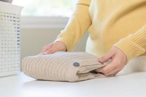 Housewife, asian young woman hand in many folding freshly shirts, sweaters or dress on desk, table after washing clean clothes and drying, making household working in room at home. Laundry and maid. photo