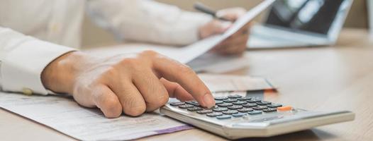 Close up hand of stress asian young businessman, male pressing a calculator to calculate tax income and expenses, bills, credit card for payment or payday at home, office.Financial, finance concept. photo