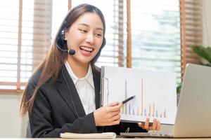 operador, asiático joven mujer vistiendo auriculares, auriculares y Hablando en vídeo llamada conferencia con cliente, colegas apoyo teléfono, trabajo en ordenador portátil tecnologia computacional de ayuda, consultar Servicio foto