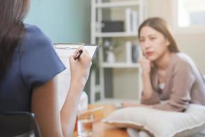 psicología, depresión. triste, sufrimiento asiático joven mujer consultante con psicólogo, psiquiatra mientras paciente asesoramiento mental con médico mujer tomando notas a clínica. alentador, terapia. foto