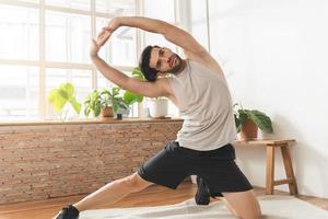 Handsome fitness caucasian young man, guy wearing sportswear training strength muscles workout, exercise training in living room at home for healthy body strong athletic, fit active lifestyle. photo