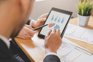 Business meeting, two caucasian, asian group man use tablet brainstorm analyzing on graph data of cost plan or document, paperwork and discussing in board room on table. People working conference room photo