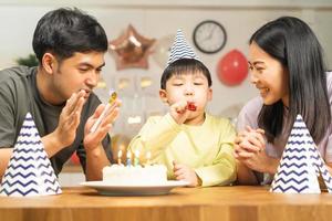 contento cumpleaños fiesta en familia, asiático joven padre padre, madre y pequeño linda chico o niño celebrando, soplo velas en el pastel y decorado globos, celebracion a hogar. encantador momentos foto