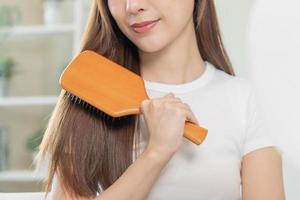 Health hair care, beauty makeup asian woman, girl holding hairbrush and brushing, combing her long straight hair looking at reflection in mirror in morning routine after salon treatment, hairstyle. photo