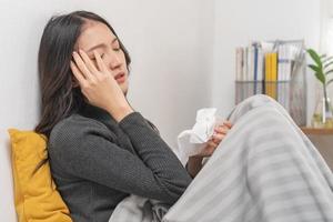 Seasonal sick, illness asian young, girl woman have headache expression weak, tired face under blanket, have a fever, use tissue paper sneezing nose, runny sitting on bed at home. Health care person.