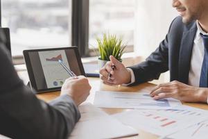 Business meeting, two caucasian, asian group man use tablet brainstorm analyzing on graph data of cost plan or document, paperwork and discussing in board room on table. People working conference room photo