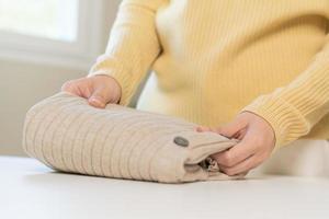 Housewife, asian young woman hand in many folding freshly shirts, sweaters or dress on desk, table after washing clean clothes and drying, making household working in room at home. Laundry and maid. photo