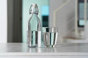 A glass of clean drinking water and a water bottle On a white wooden table photo