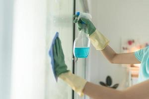 Female hand in green gloves cleaning window with blue rag and spray detergent. photo