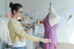 Attractive young fashion designer standing in studio holding tablet next to mannequin. photo