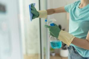 Female hand in green gloves cleaning window with blue rag and spray detergent. photo