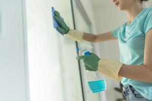 Female hand in green gloves cleaning window with blue rag and spray detergent. photo