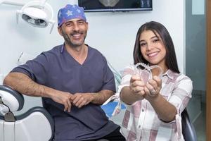 Happy ethnic teen girls showing teeth aligners near dentist in clinic photo