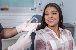 Unrecognizable dentist showing silicone aligners to positive ethnic girl photo