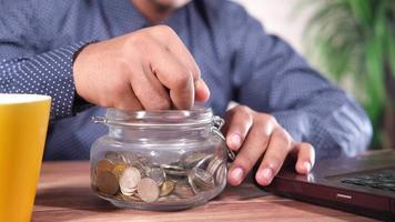 Man dropping coins into a jar on table video