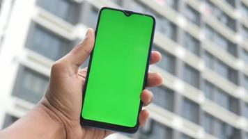 jong Mens hand- gebruik makend van slim telefoon met groen scherm tegen stad gebouwen video