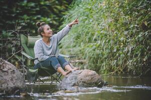 mujer joven sentada en una silla de camping en el arroyo para relajarse foto