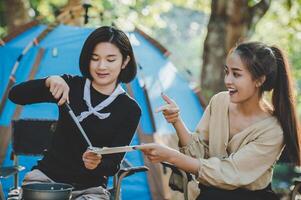 Young woman cooking with egg while camping with girl friend photo