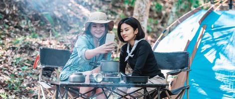 Asian pretty woman and girlfriend use smartphone selfie on camping photo