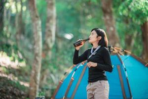 Young woman cheer and drink beverage  front of camping tent photo