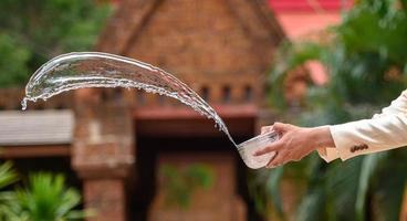 Young man splashing water from bowl on Songkran festival photo