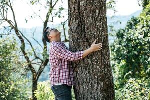 retrato de un hombre asiático feliz abrazando un árbol en el bosque foto