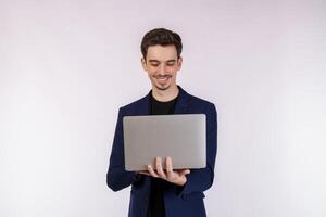 retrato de un joven y apuesto hombre de negocios sonriente sosteniendo una laptop en las manos, escribiendo y navegando por páginas web aisladas de fondo blanco foto