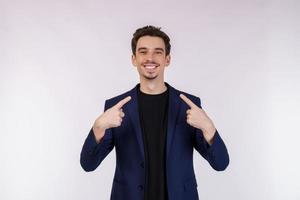 Portrait of attractive cheerful young man pointing finger at himself and standing isolated over background photo